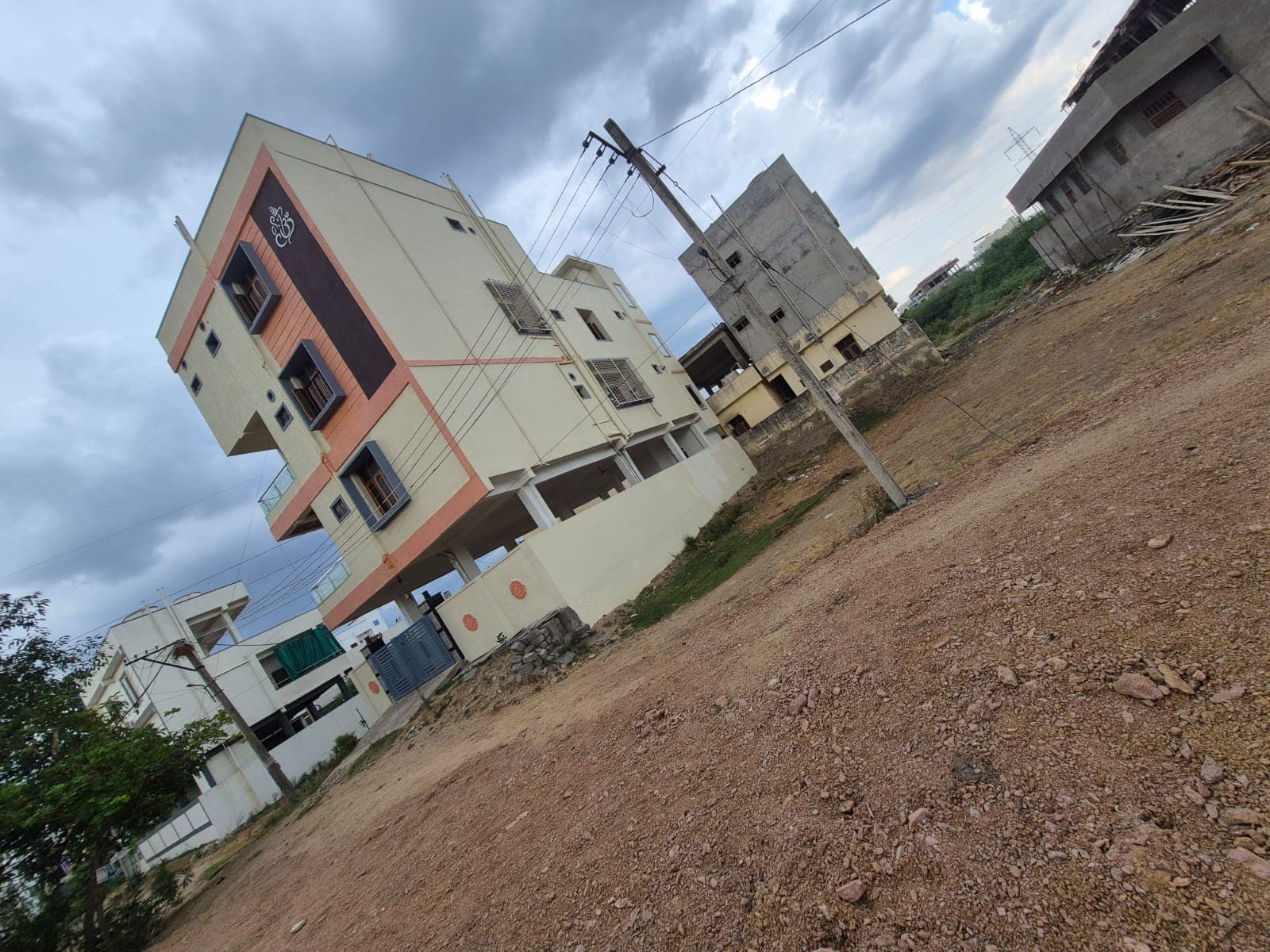 Modern yellow and brown multi-story house on a dirt lot under a cloudy sky.