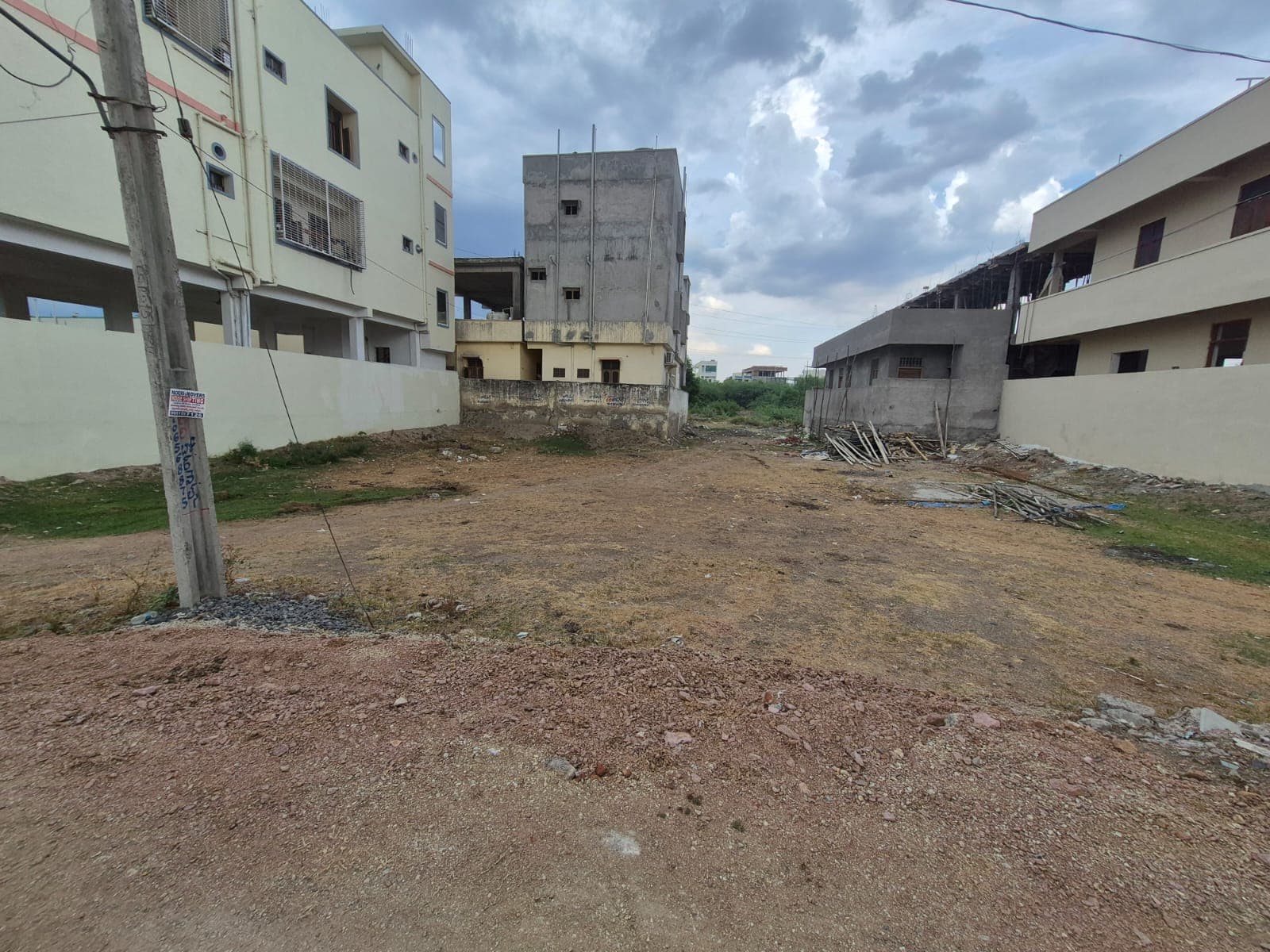 A vacant dirt lot surrounded by several multi-story buildings under a cloudy, overcast sky.